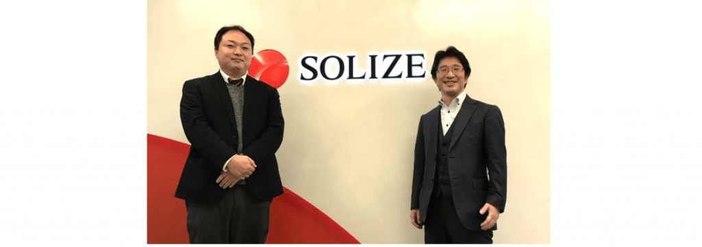SOLIZEの文字を背景に立つ男性二人